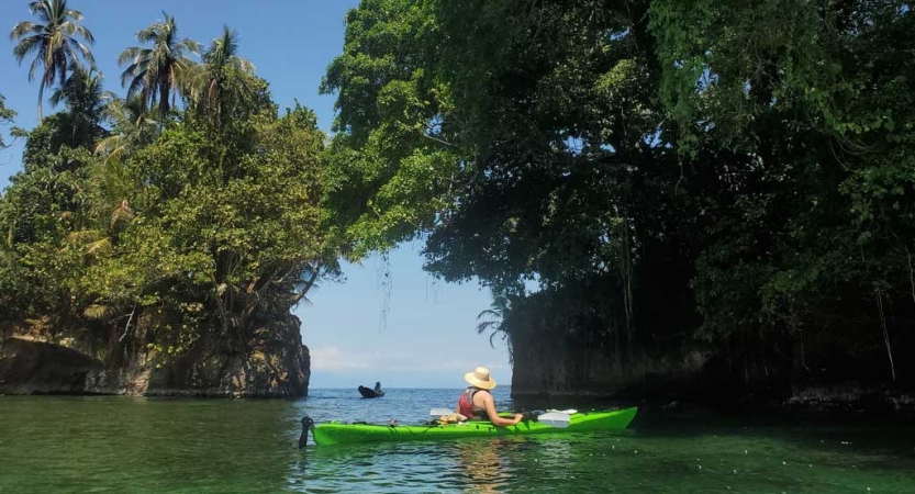 A person paddles a green kayak on calm water in between two bodies of land